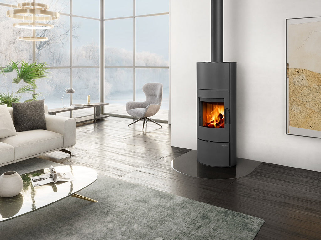Sobă pe lemne neagră cu design minimalist și evacuare verticală, amplasată pe suport de sticlă într-un living modern cu ferestre mari și vedere spre un peisaj de iarnă.