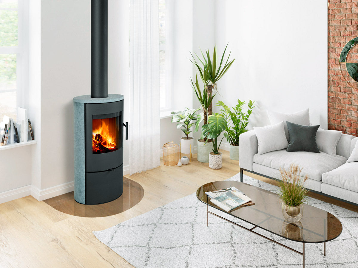 Sobă pe lemne cu finisajpiatra gri și design oval, amplasată într-un living luminos cu plante de interior și perete decorativ din cărămidă.
