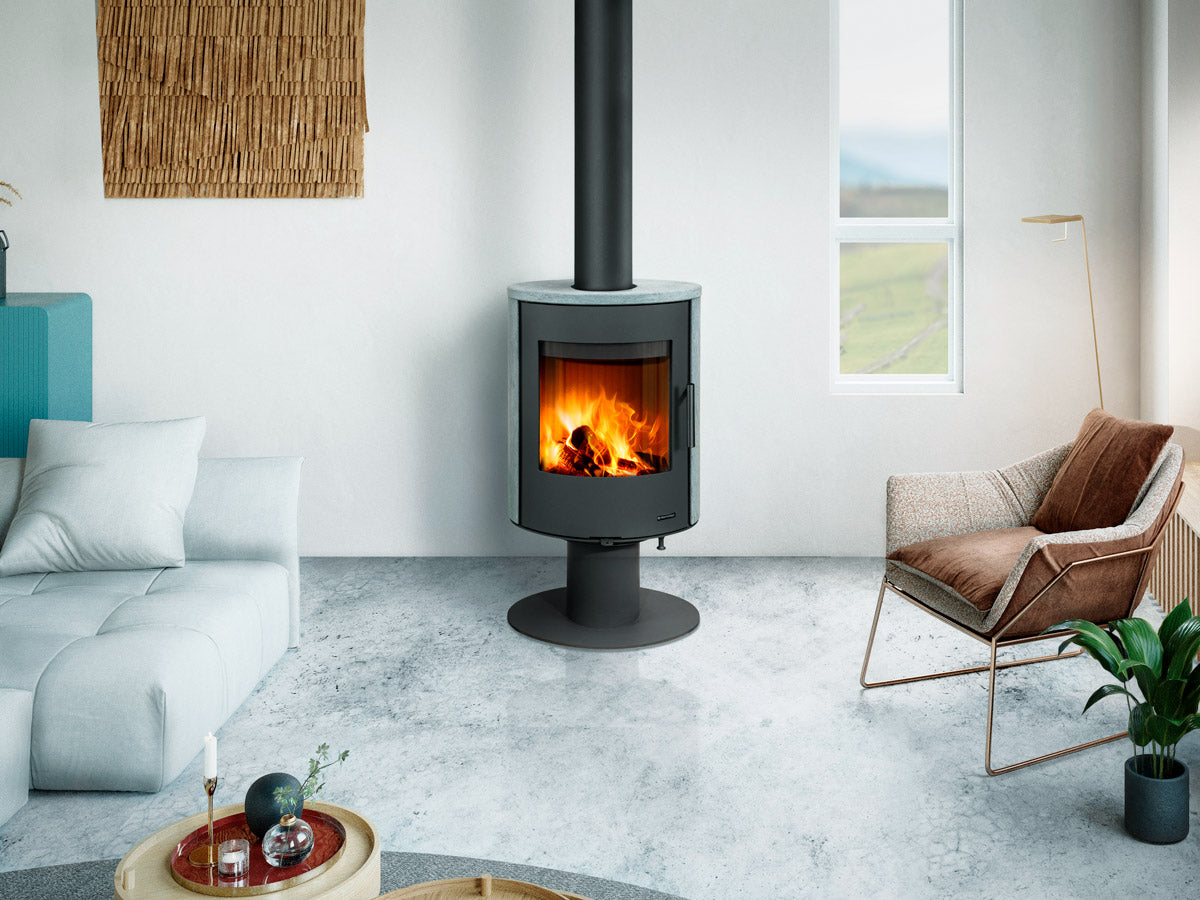 Sobă pe lemne Evora T 20 suspendată pe picior central cu finisaj gri piatră, amplasată într-un living modern cu podea din beton slefuit și decor minimalist. 