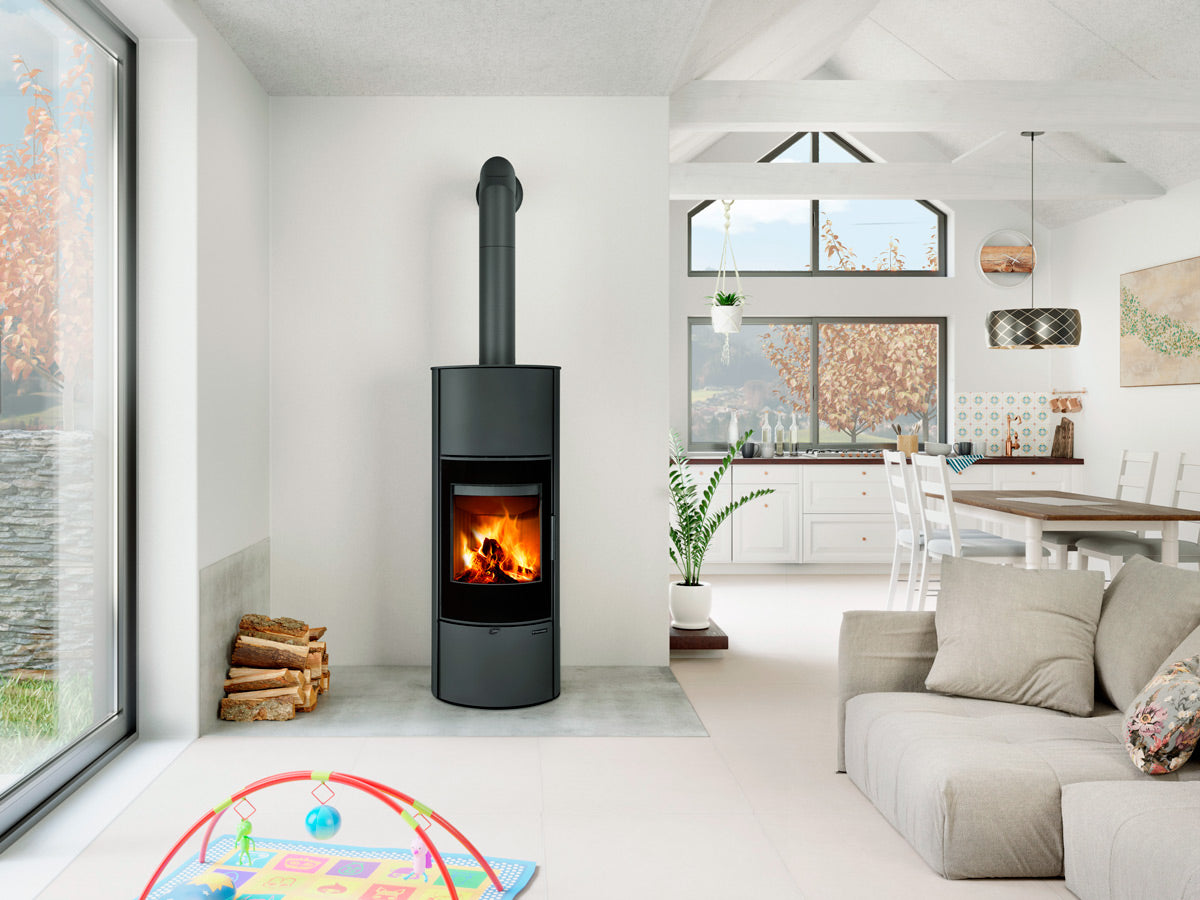 Soba pe lemne Laredo neagra, cilindrica, instalata intr-un living alb tip open space, cu zona de dining, ferestre mari si decor de toamna primitor.