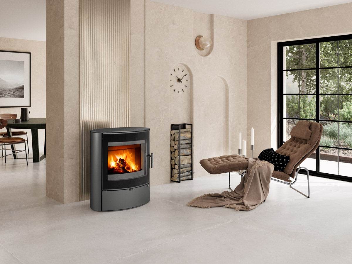 Soba metalica Navia G cu design oval, amplasata intr-un living minimalist bej cu sezlong confortabil, zona de relaxare si ferestre mari negre.