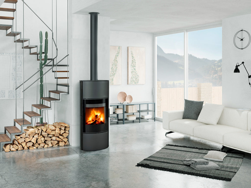 Soba ceramica Ovalis G H , cilindrica moderna cu geam panoramic si foc vizibil, instalata in living contemporan luminos, cu cos de fum vertical si depozitare lemne decorativa.