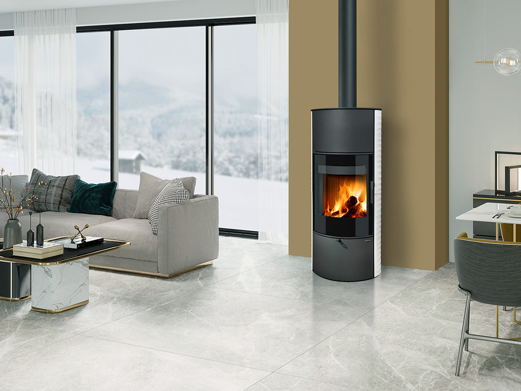 Soba pe lemne Ovalis G H , moderna, cilindrica cu geam mare frontal si foc vizibil, instalata intr-un living contemporan luminos cu ferestre panoramice si design elegant.