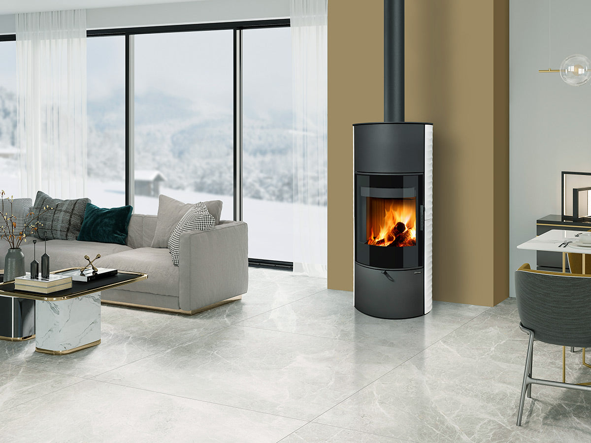 Soba pe lemne Ovalis G H , moderna, cilindrica cu geam mare frontal si foc vizibil, instalata intr-un living contemporan luminos cu ferestre panoramice si design elegant.