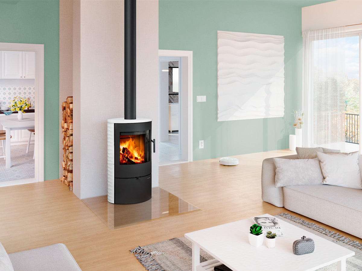 Soba lemne cilindrica placata cu ceramica alba pe lateral in relief, montata intr-un décor luminos pe un perete cu nisa pentru depozitare lemne