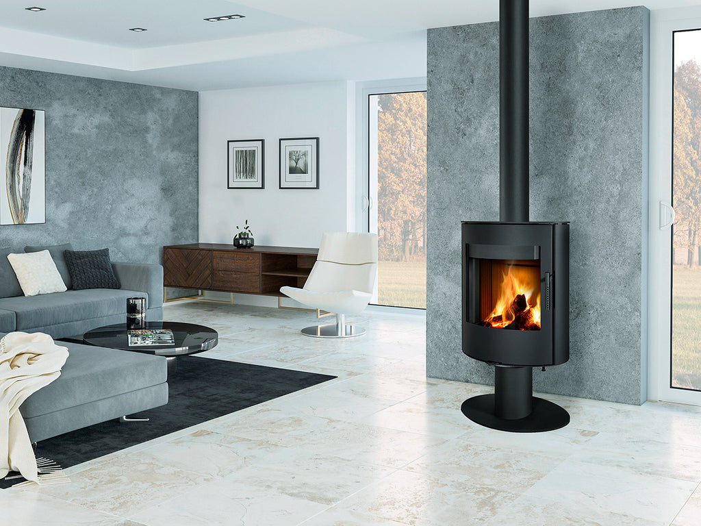 Soba metalica rotativa pe picior Ovalis T 30, cu geam curbat frontal si foc vizibil, instalata in living contemporan cu perete decorativ din beton si ferestre inalte.