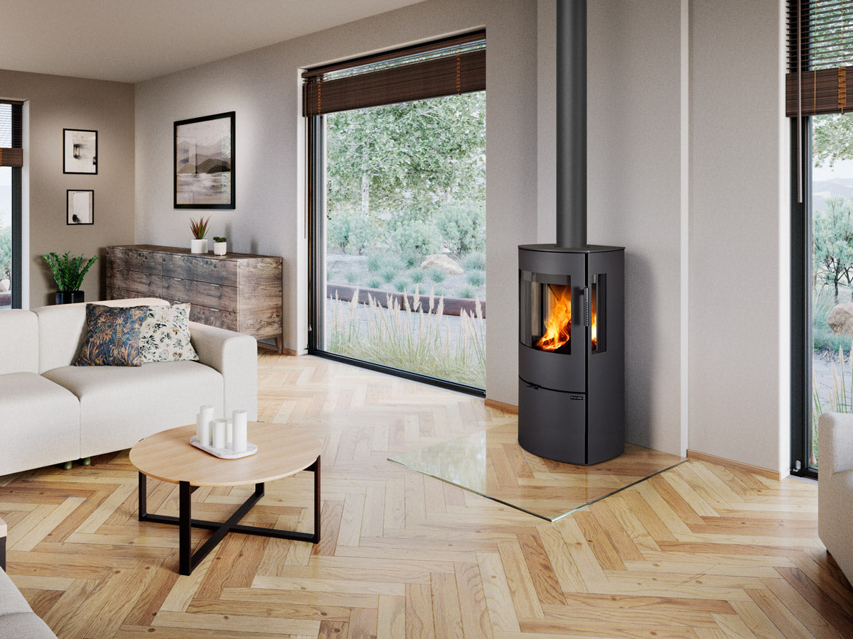 Soba pe lemne moderna cilindrica cu geam lateral si frontal pentru vizibilitate panoramica a focului, instalata intr-un living contemporan luminos cu ferestre mari.