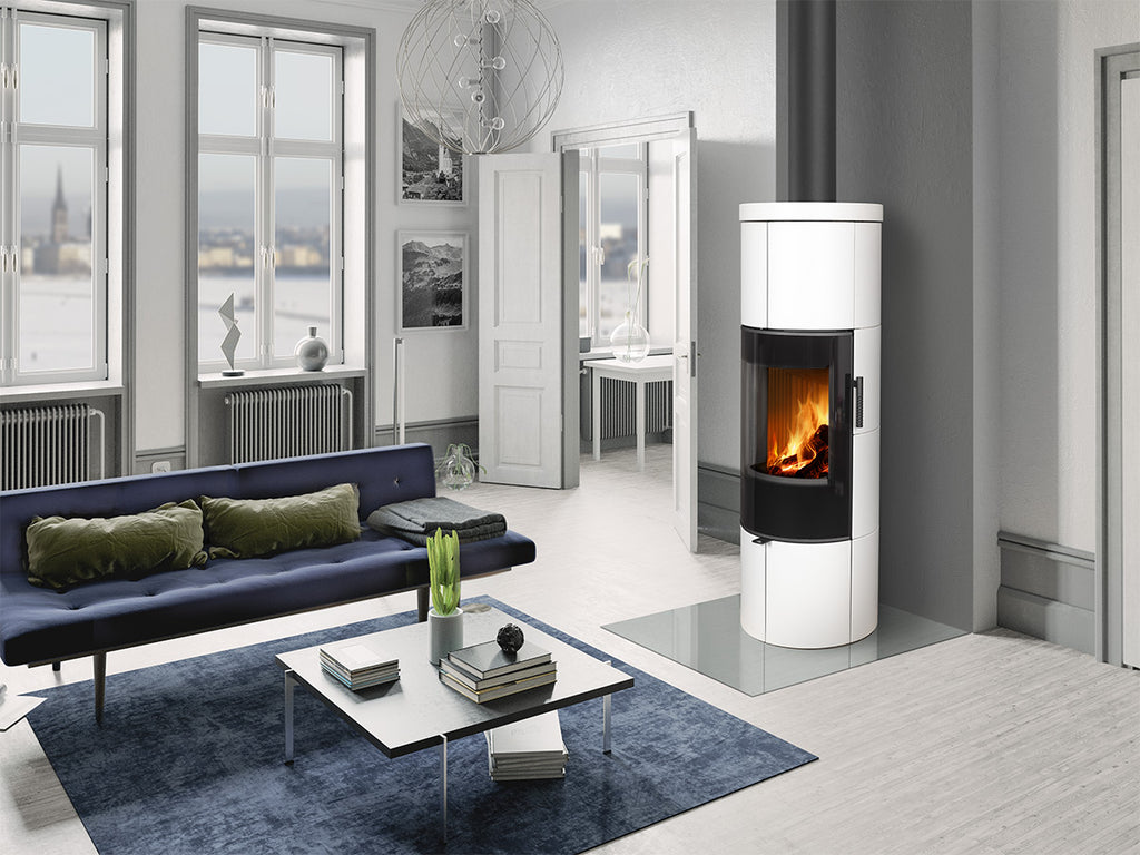 Soba lemne SORIA H 10, cilindrica, alba, cu usa de sticla neagra, foc vizibil si cos de fum. Amplasata intr-un living modern.