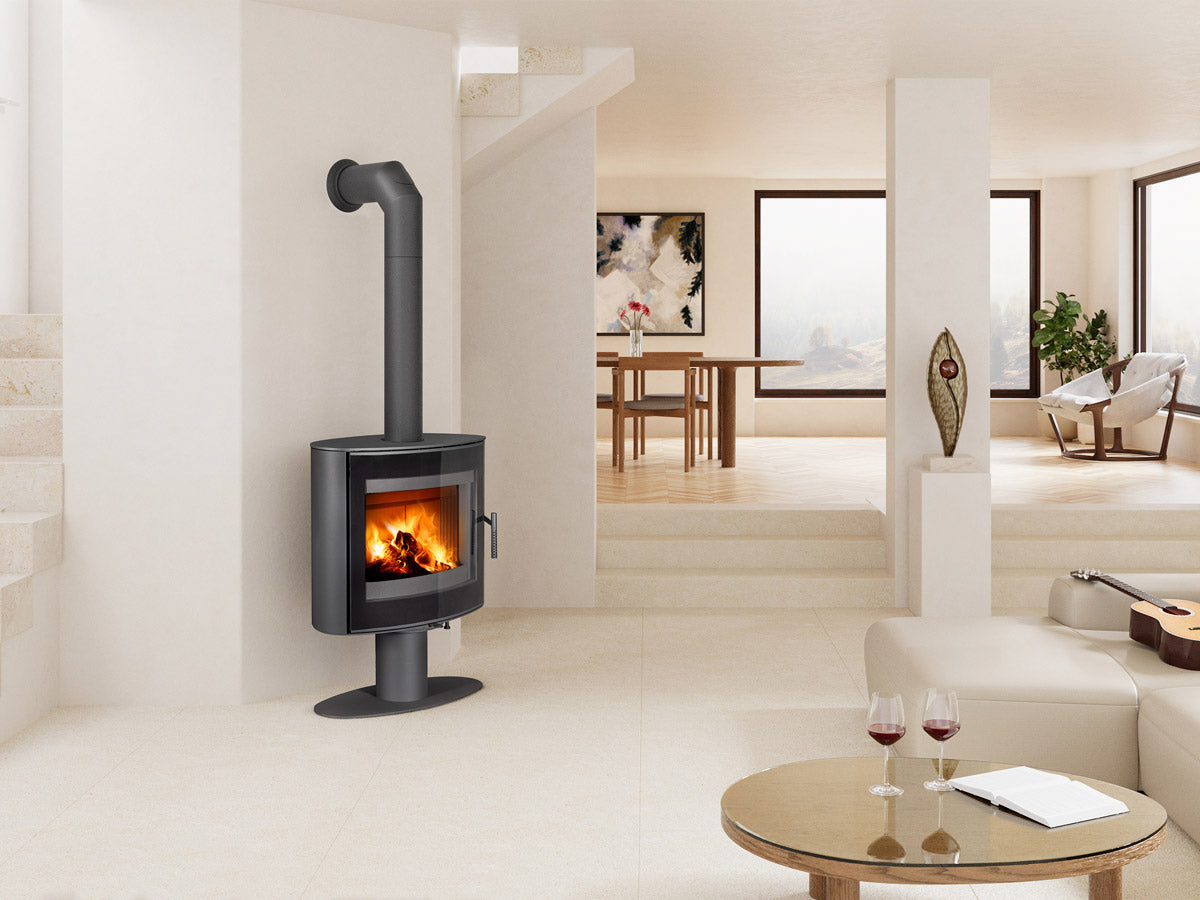 Soba lemne STROMBOLI T 30, metal gri inchis, forma curbata, cu usa mare de sticla, foc vizibil si burlan. Amplasata in living modern.