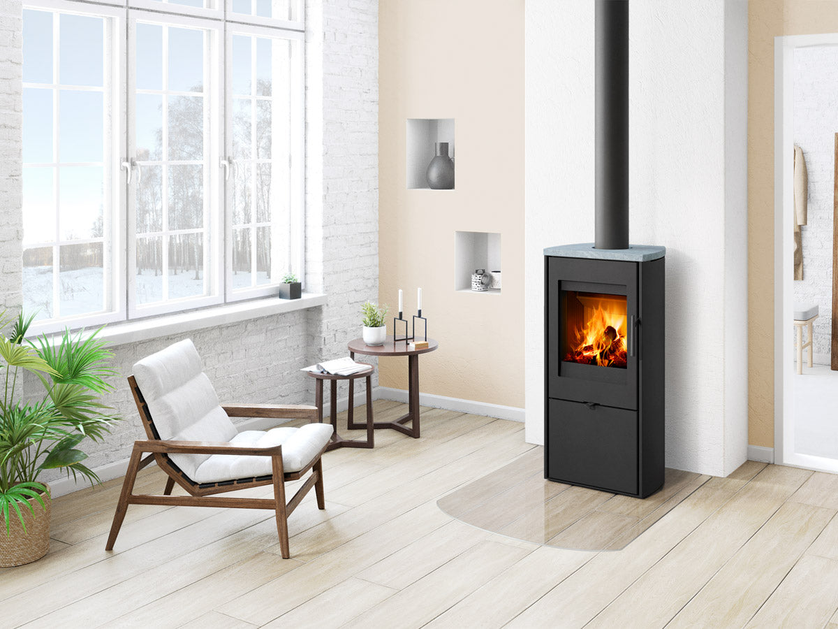Soba lemne TALA 20, metal negru, forma cubica, cu blat gri, geam frontal cu foc vizibil si cos. Amplasata intr-un living modern, luminos.
